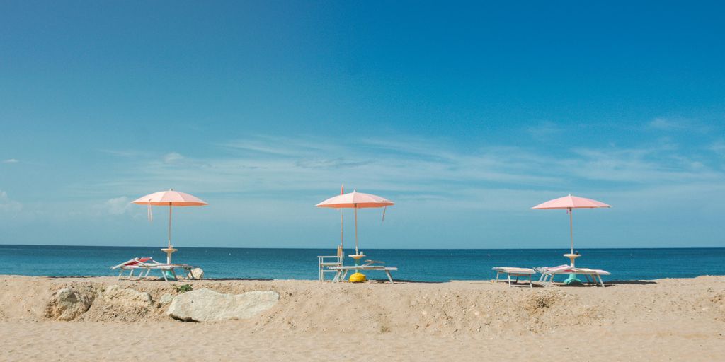 three empty beach loungers with umbrellas overlooking the beach under blue sky